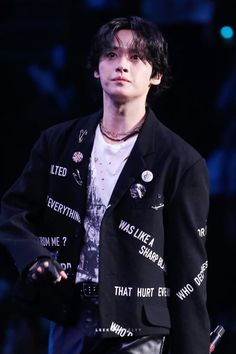 a young man in a black jacket and white t - shirt with words on it