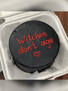 a black cake with red writing on it sitting in a white box that says witches don't age