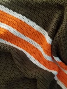 an orange and white crocheted blanket laying on top of a bed next to a pillow