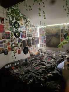 an unmade bed with lots of pictures on the wall and plants hanging from the ceiling