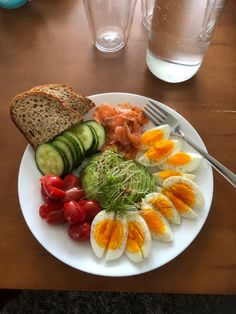 a white plate topped with eggs, tomatoes and cucumbers next to a slice of bread