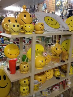 many yellow smiley faces are on shelves in a store with cups and mugs behind them