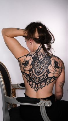 a woman sitting in a chair with her back to the camera and tattoos on her body