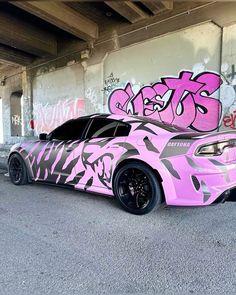 a pink car covered in graffiti parked under a bridge