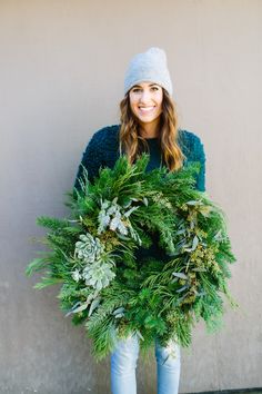 a woman is holding a wreath with greenery on it