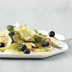 a white plate topped with salad and blueberries on top of a table next to a fork