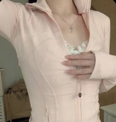 a woman wearing a pink jacket and white shirt is holding her hands on her chest