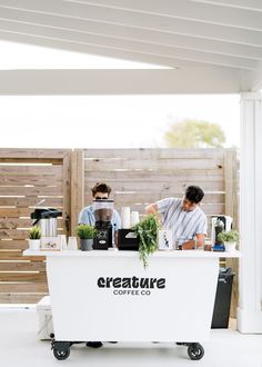 two men sitting at a table with plants in front of them and the words creature coffee co on it