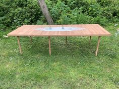 a wooden table sitting on top of a grass covered field next to a tree and bushes