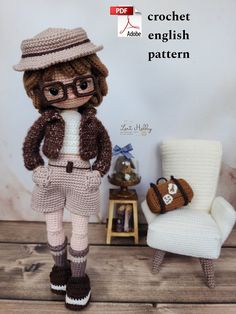 a crochet doll is standing next to a chair and purse on a wooden table