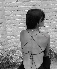 a woman sitting on the ground with her back to the camera and tattoos on her body