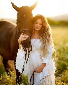 a pregnant woman standing next to a brown horse