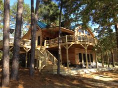 a large wooden house surrounded by trees in the middle of a forest with stairs leading up to it's second story