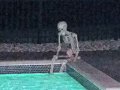 a skeleton sitting on the edge of a swimming pool