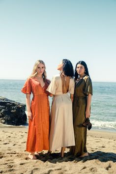 three women standing next to each other on a beach