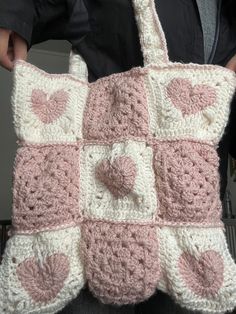 a crocheted pink and white tote bag with hearts on the front is being held by a woman