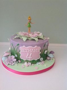 a birthday cake with a tinkerbell figure on top and flowers around the edges