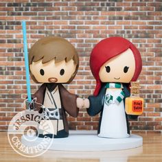 star wars wedding cake topper with luke and princess leion holding hands, on wooden table next to brick wall