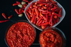 two bowls filled with red chili paste next to some peanuts and other food items on a black surface