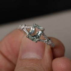 a person holding a ring with an aquamarine colored stone and diamonds on it's sides