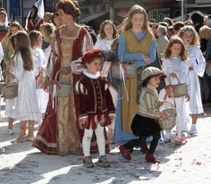 several children dressed in medieval costumes standing next to each other on the street with people watching