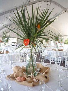 a vase filled with flowers sitting on top of a white tablecloth covered banquet tables