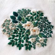 an embroidered piece of cloth with white flowers and green leaves