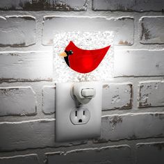 a red bird sitting on top of a white light switch cover next to a brick wall