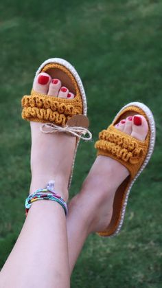 a woman's feet wearing yellow crochet sandals and bracelets in the grass