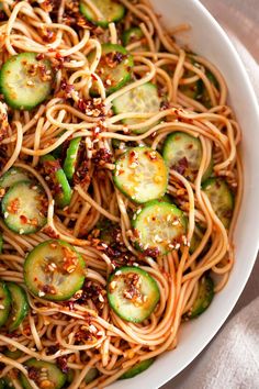 a white bowl filled with noodles, cucumbers and sesame seed sprouts