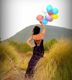 a woman in a purple dress holding balloons up to the sky while standing on top of a hill