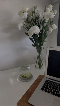 a vase with white flowers sitting next to a laptop