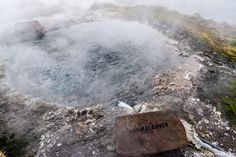 a hot spring in the middle of a mountain with steam rising from it's surface