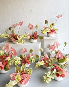 several white vases with pink and green flowers in them on top of a table