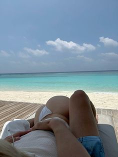 a woman laying on top of a wooden deck next to the ocean with her legs crossed