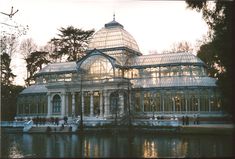 a large glass building sitting on top of a lake next to a forest filled with trees