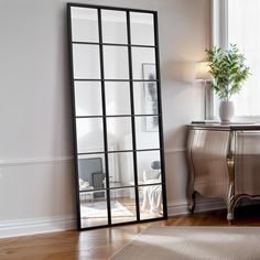 a large mirror sitting on top of a wooden floor next to a table with a potted plant