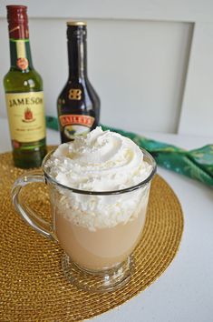 a glass cup filled with whipped cream next to two bottles of booze and a straw hat