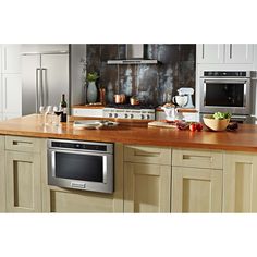 a modern kitchen with stainless steel appliances and wood counter tops, including an oven, microwave, dishwasher, wine glass and bottle on the island