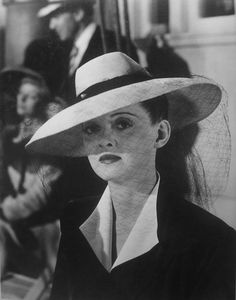 black and white photograph of woman in large hat with other people behind her looking on