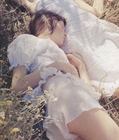 a woman is laying in the grass with her eyes closed and she is wearing a white dress