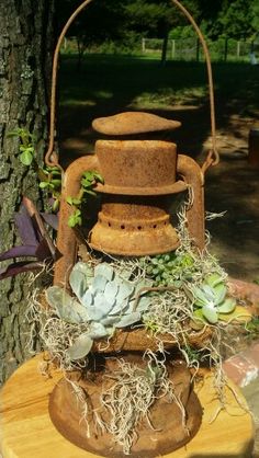 an old iron lantern with succulents and moss on it sits in front of a tree