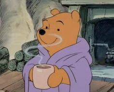 a winnie the pooh character holding a coffee cup in front of a fire place