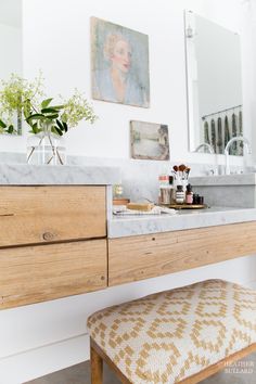 a bathroom vanity with a stool and painting on the wall above it, in front of a large mirror