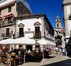 people sitting at tables in front of an old building with white umbrellas on the street