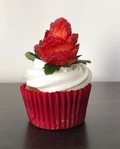 a red cupcake with white frosting and a strawberry on top is sitting on a table