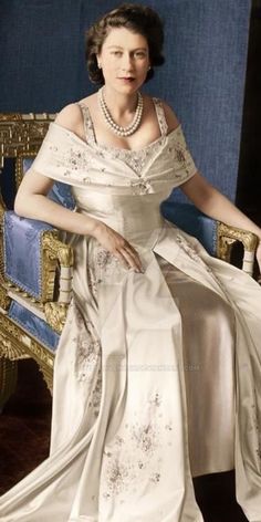 an old photo of a woman in a white dress sitting on a blue chair wearing pearls