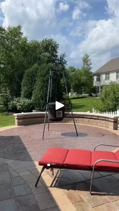 a red lounge chair sitting on top of a brick patio next to a swing set