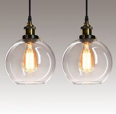 two clear glass pendant lights hanging from a black wire and one light bulb is turned on