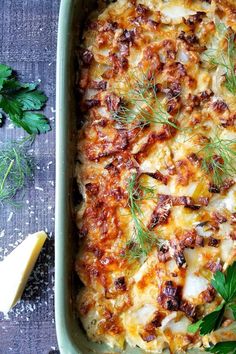 a casserole dish with cheese, meat and fresh herbs on the table next to some parsley